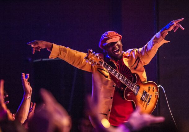 Musician performing energetically on stage with guitar.
