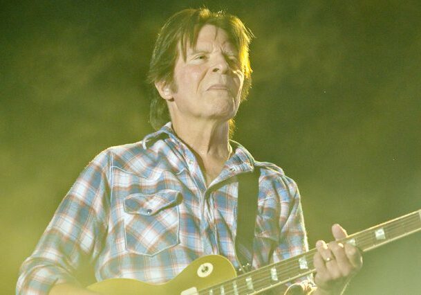 Musician playing guitar under stage lights.