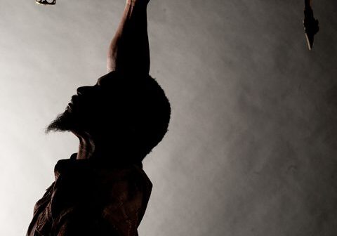 Silhouette of person holding saxophone overhead.