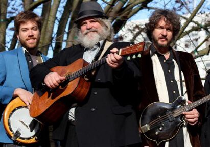 Five musicians posing with instruments outdoors.