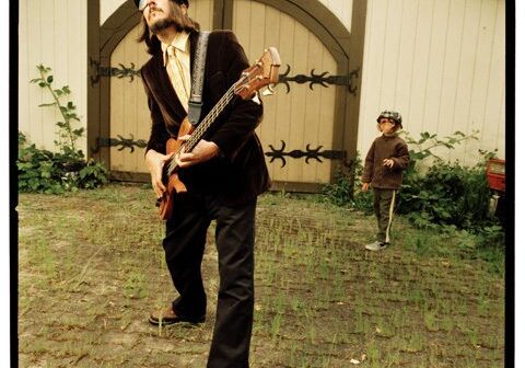 Man playing guitar outside, child in background.