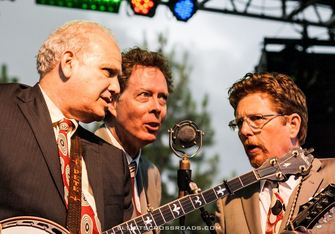 Three musicians performing with banjos on stage.