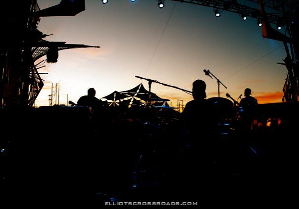 Silhouetted band performing at outdoor festival.