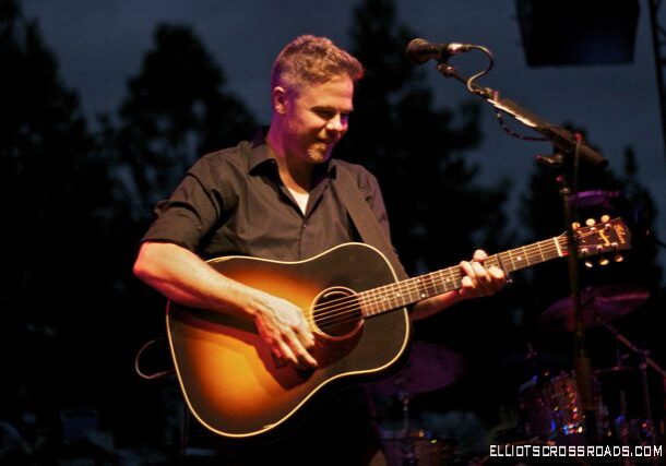 Musician playing guitar on stage at night.