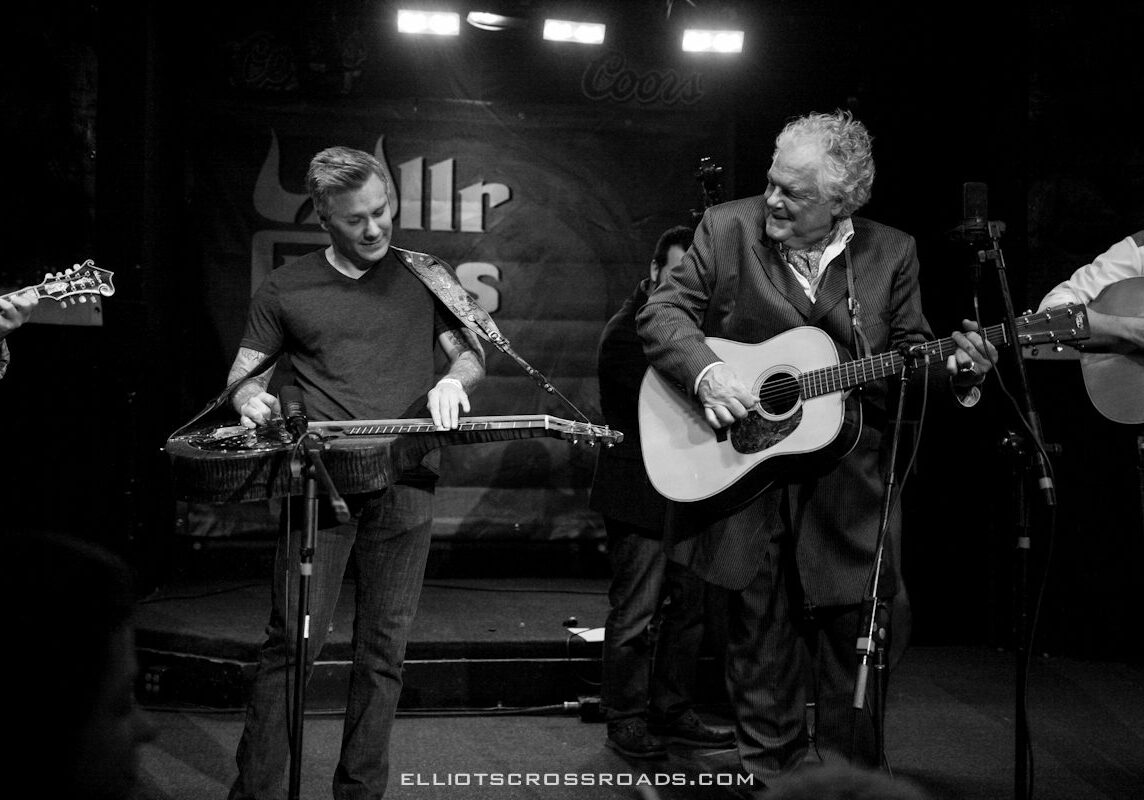 Musicians playing guitars on stage, smiling, performing.