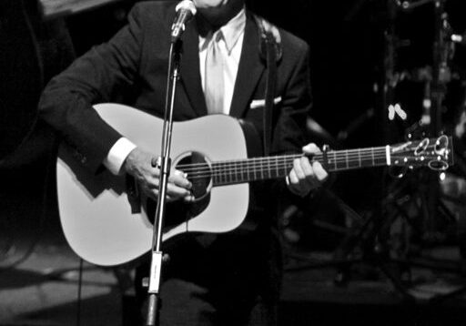Man playing guitar on stage, smiling.