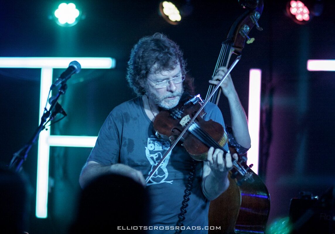 Musician playing violin on stage with lights.