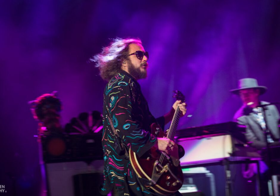 Musician playing guitar on stage with band.