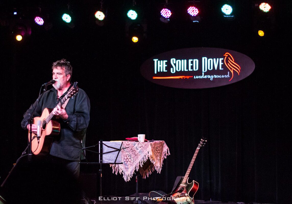 Musician performing on stage with guitar.