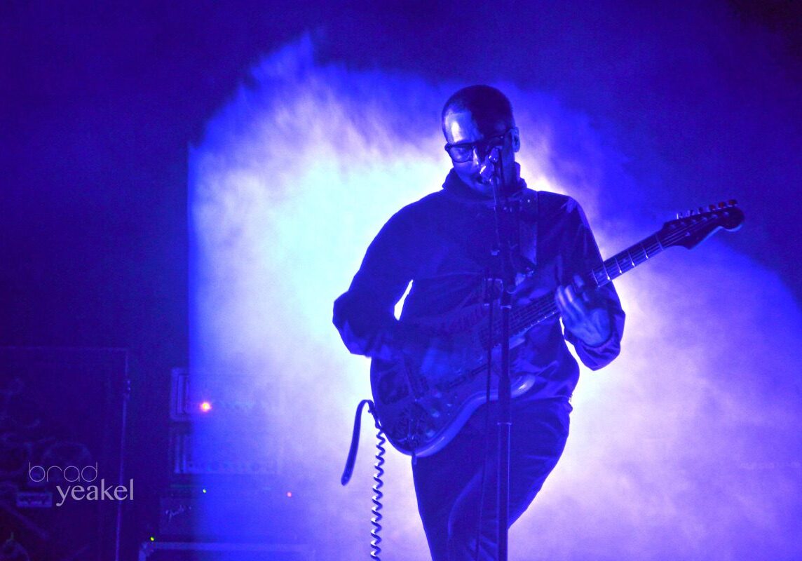 Guitarist performing on stage with blue lighting.