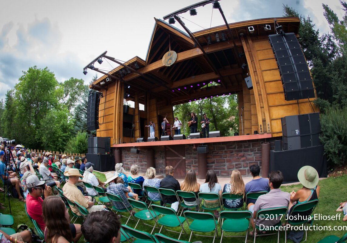 Outdoor concert with audience and wooden stage.