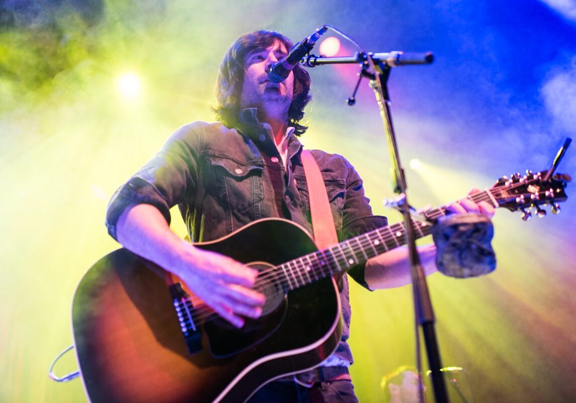 Musician playing guitar under colorful stage lights.