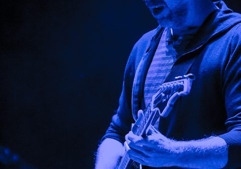 Musician playing guitar on stage, blue lighting.