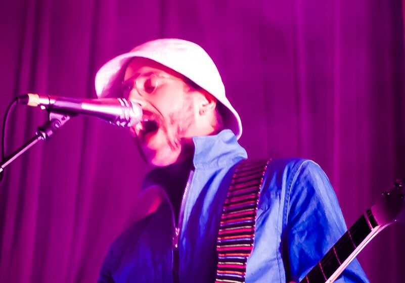 Musician singing passionately on stage, purple lighting.