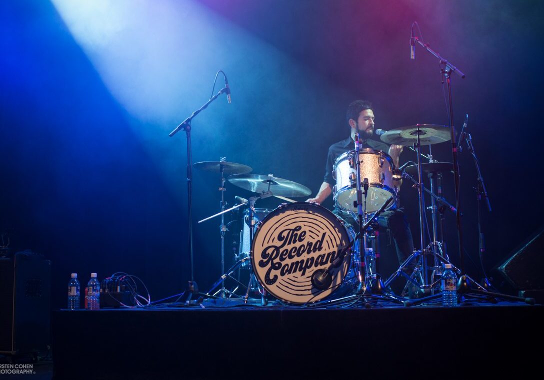 Drummer performing on stage with blue lights.