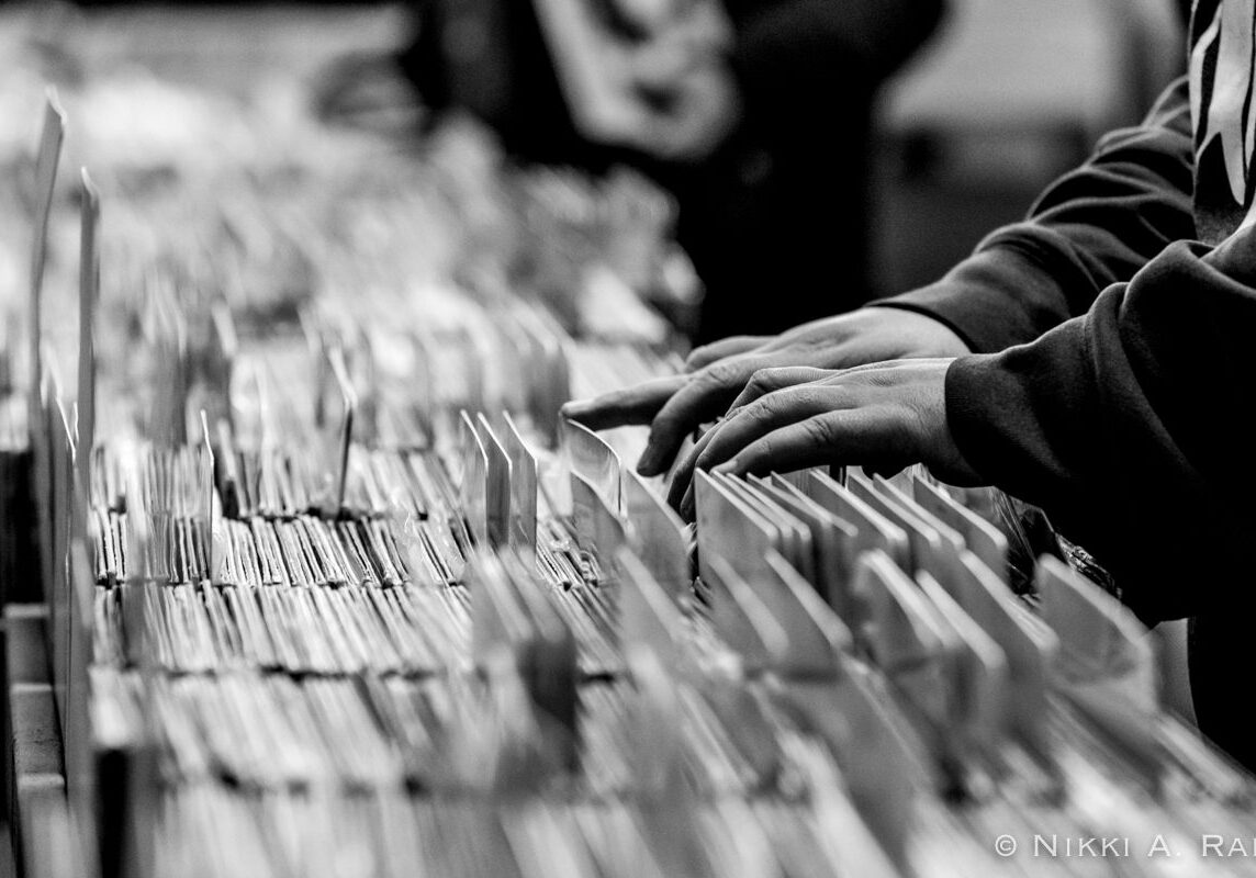 Hands browsing records in a store aisle.