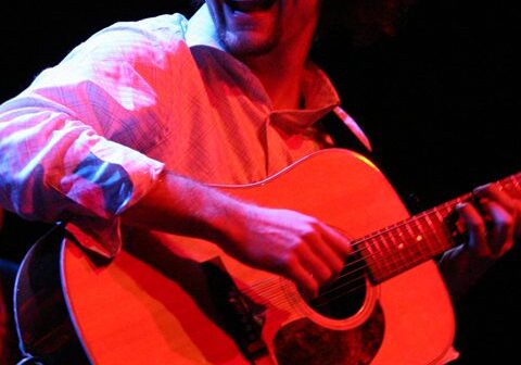 Musician joyfully playing acoustic guitar on stage.