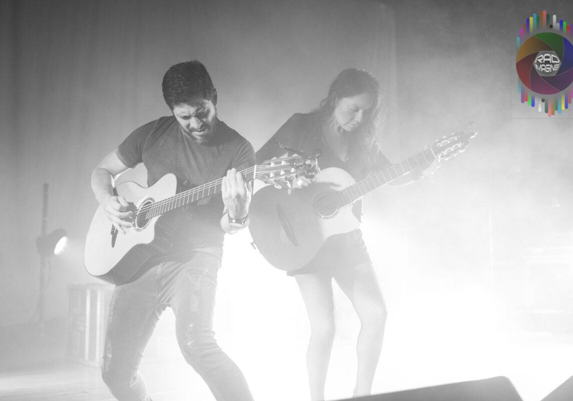 Musicians playing guitars on stage, dramatic lighting.
