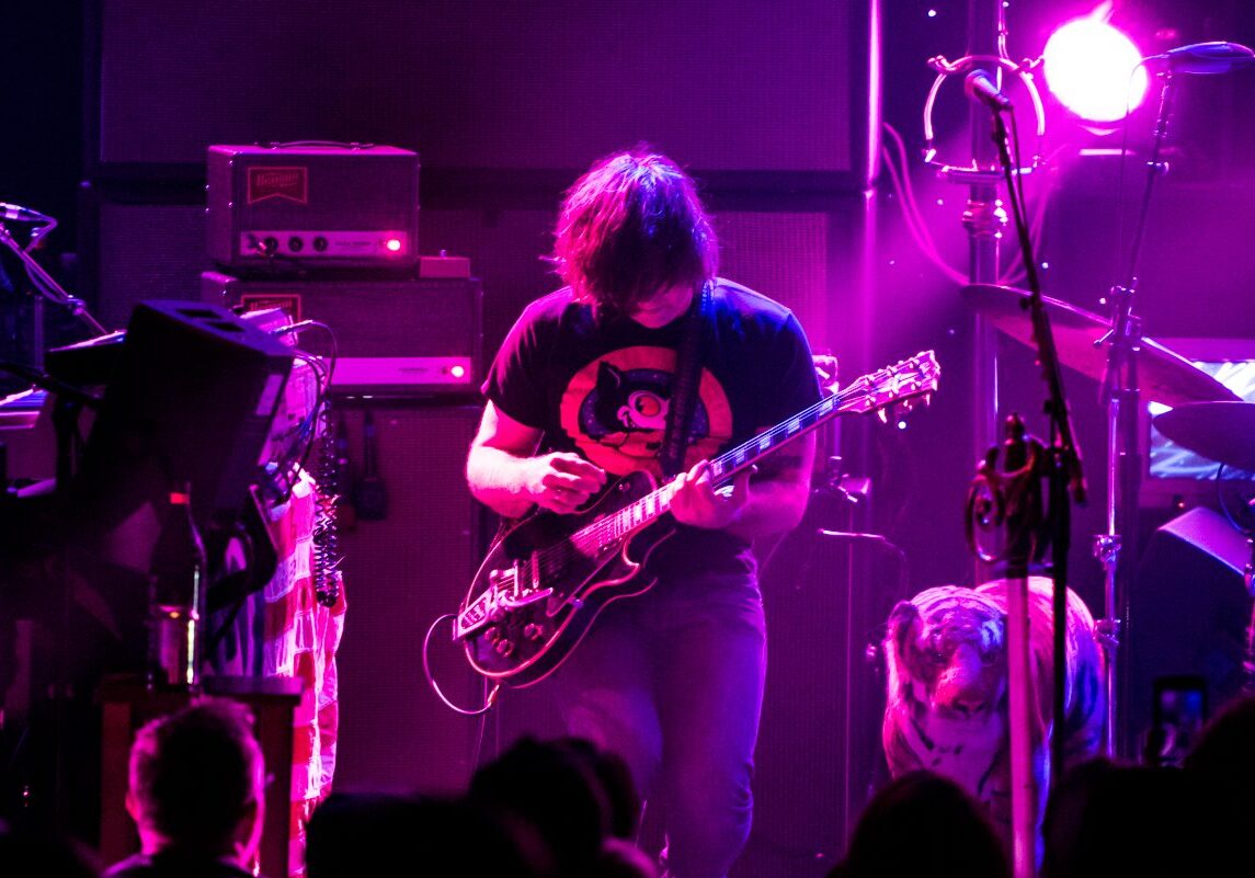 Guitarist performing on stage with vibrant lighting.
