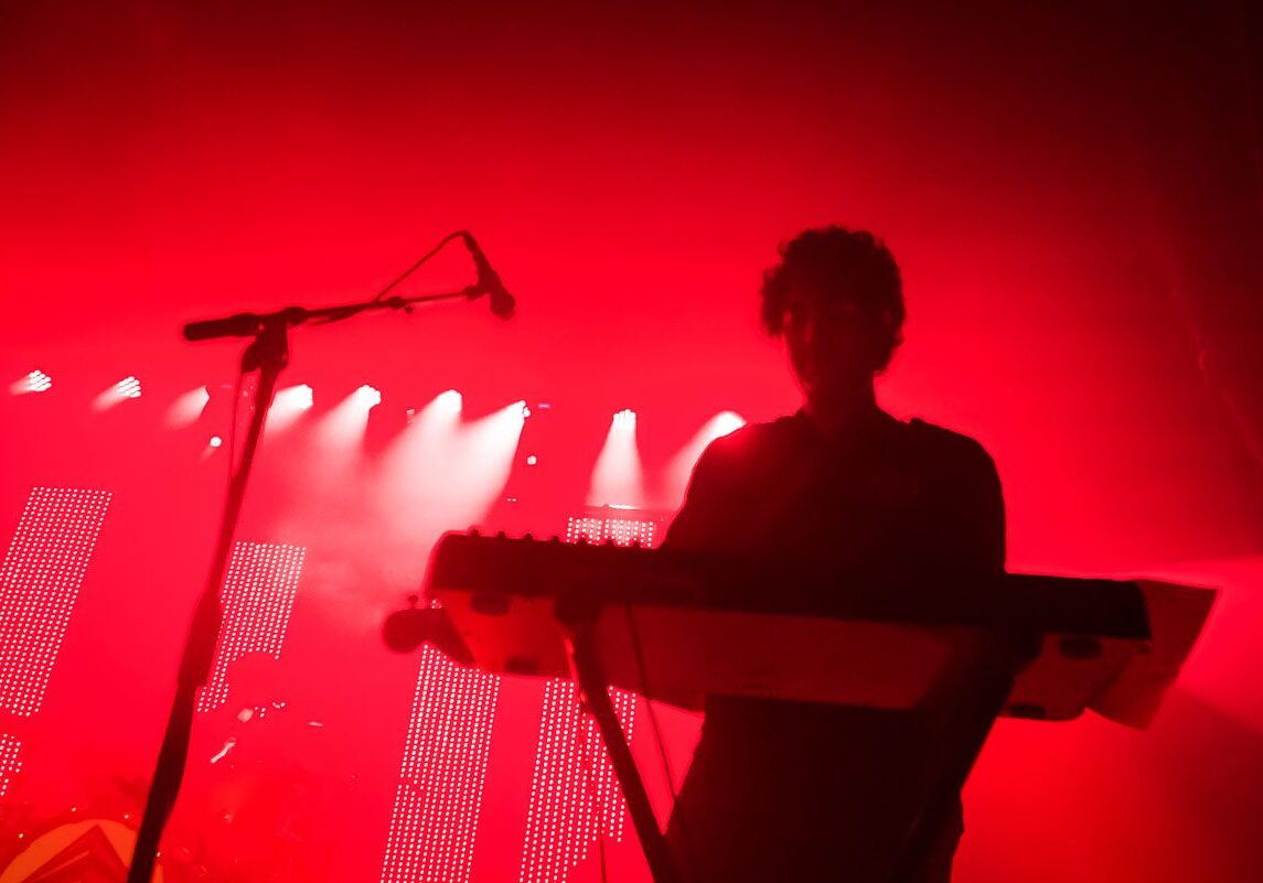 Musician performing on stage with red lighting.
