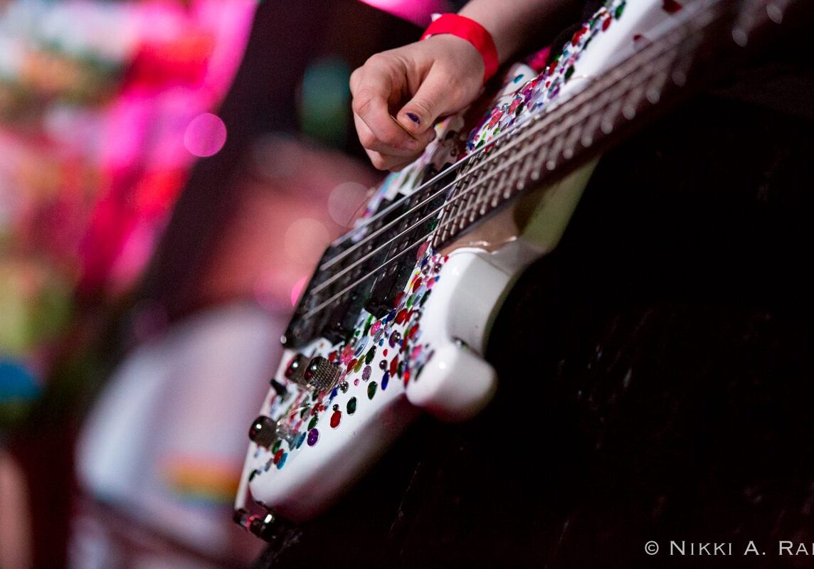Hand playing a decorated electric guitar.
