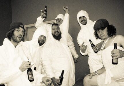 Group in costumes holding beer bottles, celebrating.