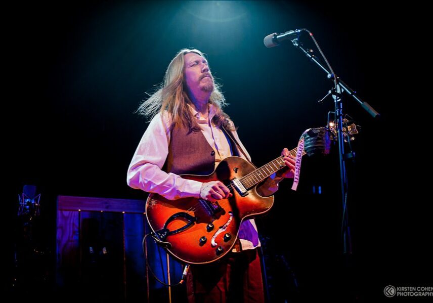 Guitarist performing on stage under spotlight.