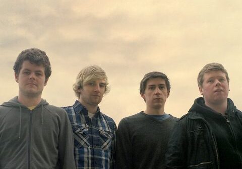 Four men standing against a cloudy sky.