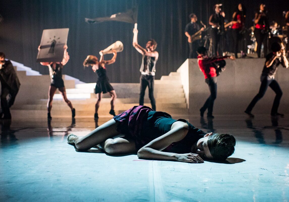 Dancer on stage with performers in background.