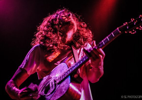 Musician playing guitar under colorful stage lights.