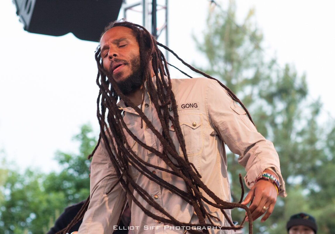 Musician performing outdoors with long dreadlocks.
