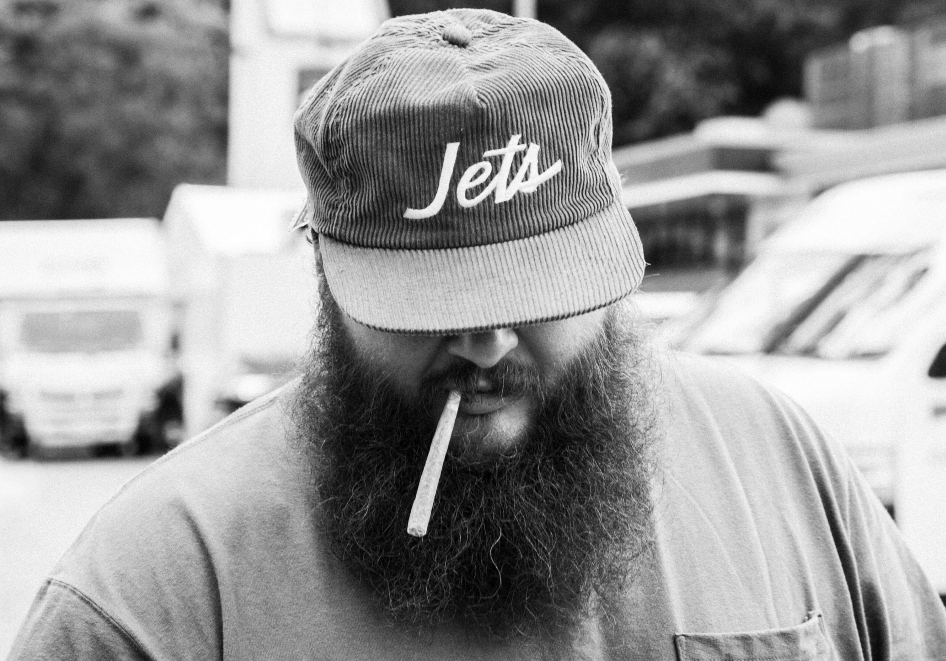Man with beard, cap, smoking cigarette.