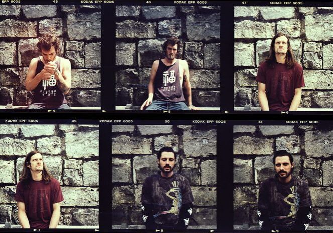 Six men posing against a stone wall.