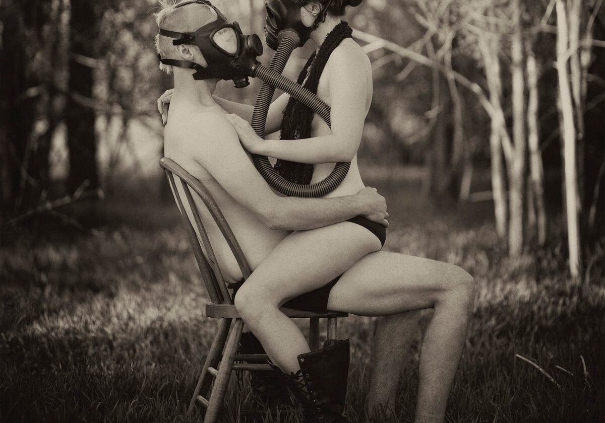 Two people sitting, wearing gas masks.