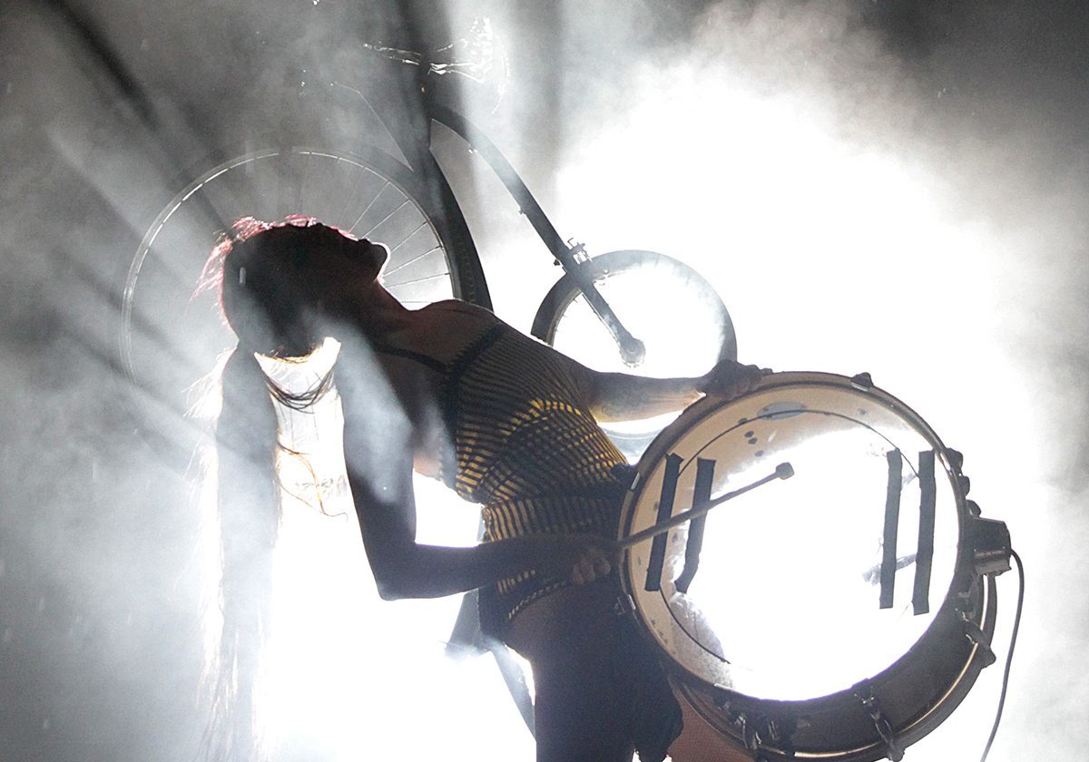 Performer with drum silhouetted against bright light.