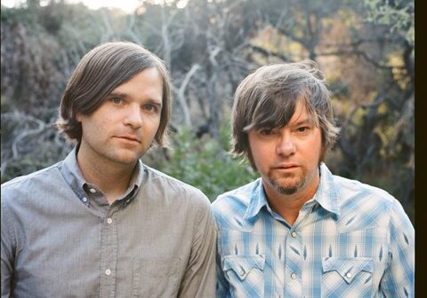 Two men standing outdoors in casual shirts.
