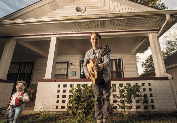 Man playing guitar in front of house.