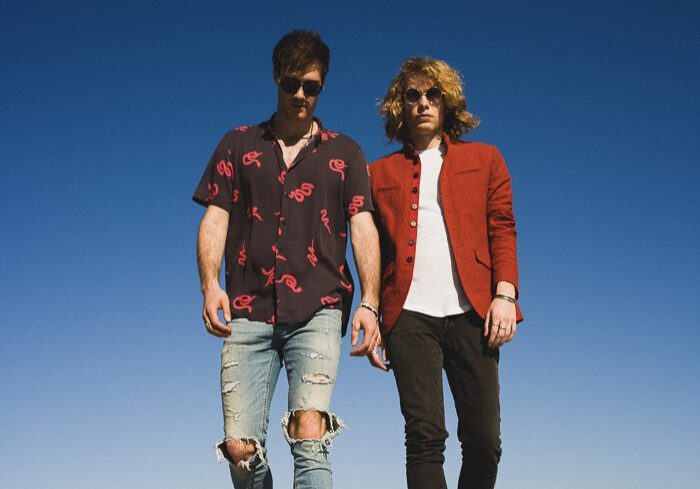 Two men walking under clear blue sky.