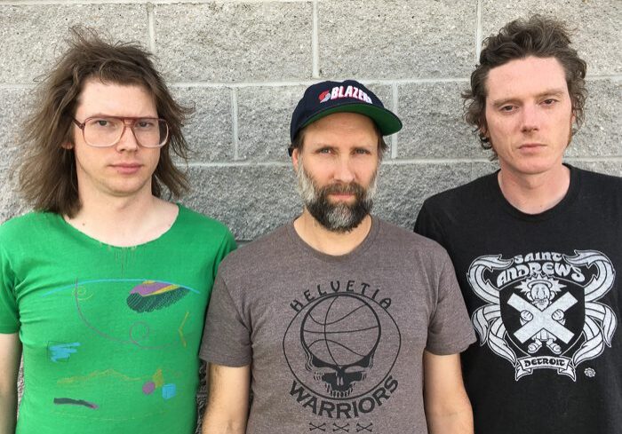 Three men standing against a brick wall.