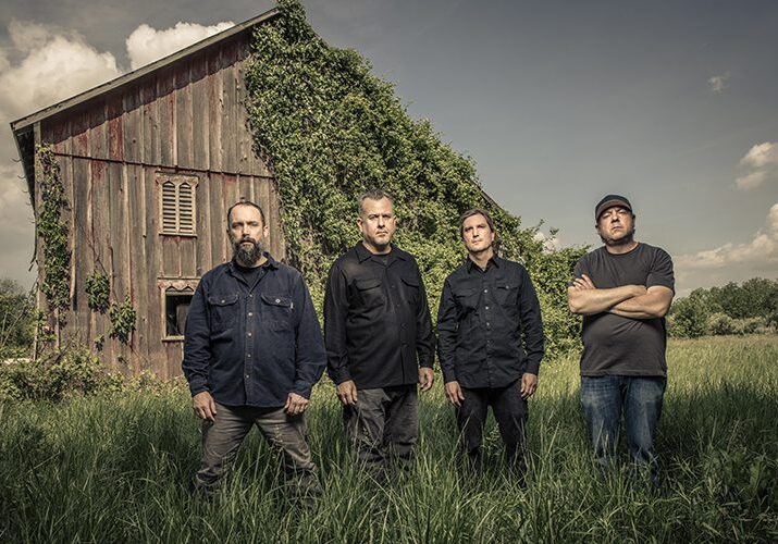 Four men standing by an ivy-covered barn.