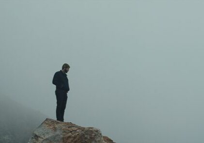 Man standing on foggy cliff edge.