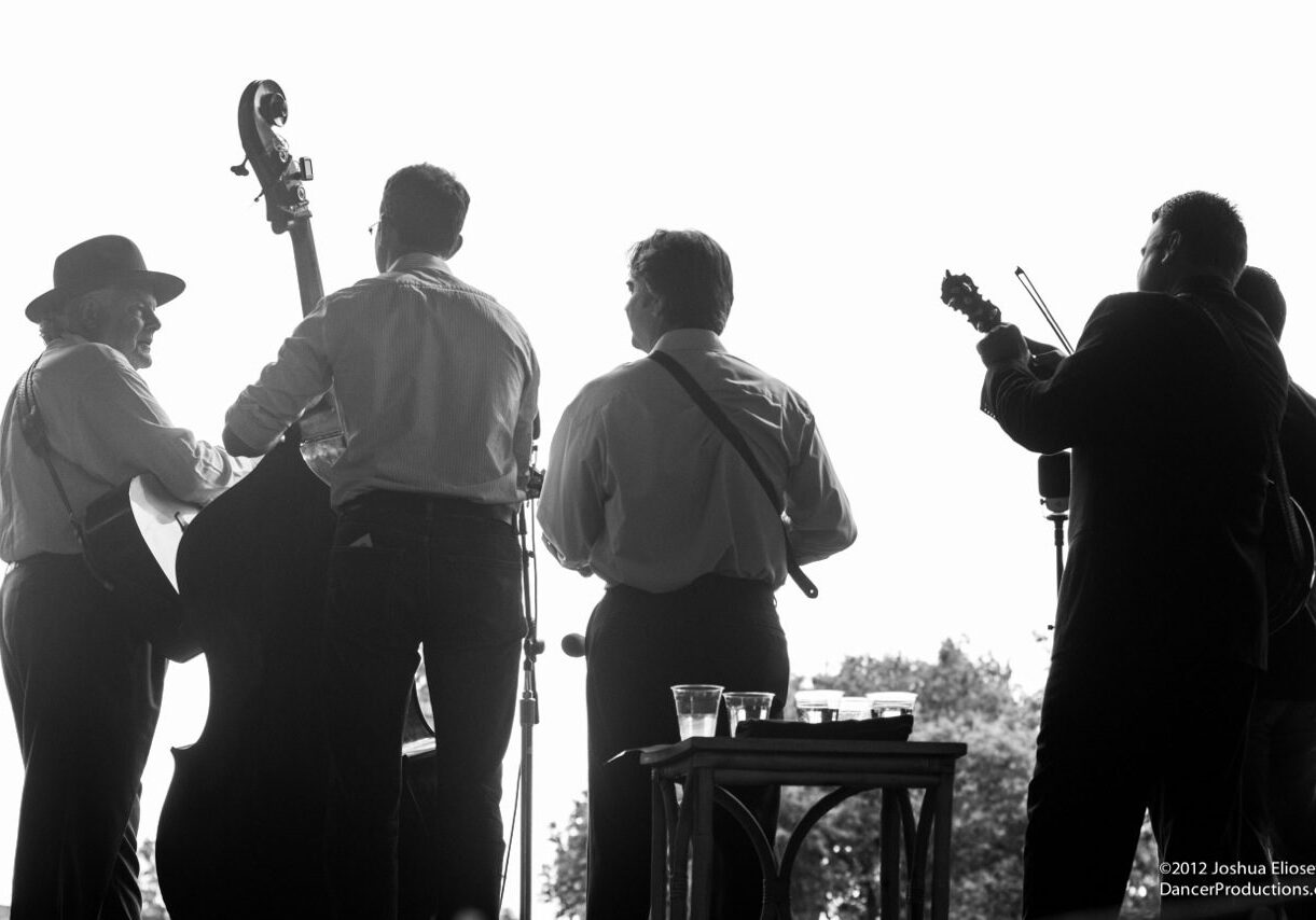 Silhouetted musicians playing on stage outdoors.