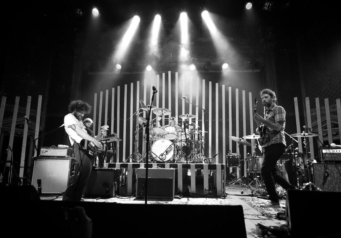 Band performing energetically on stage, black-and-white.
