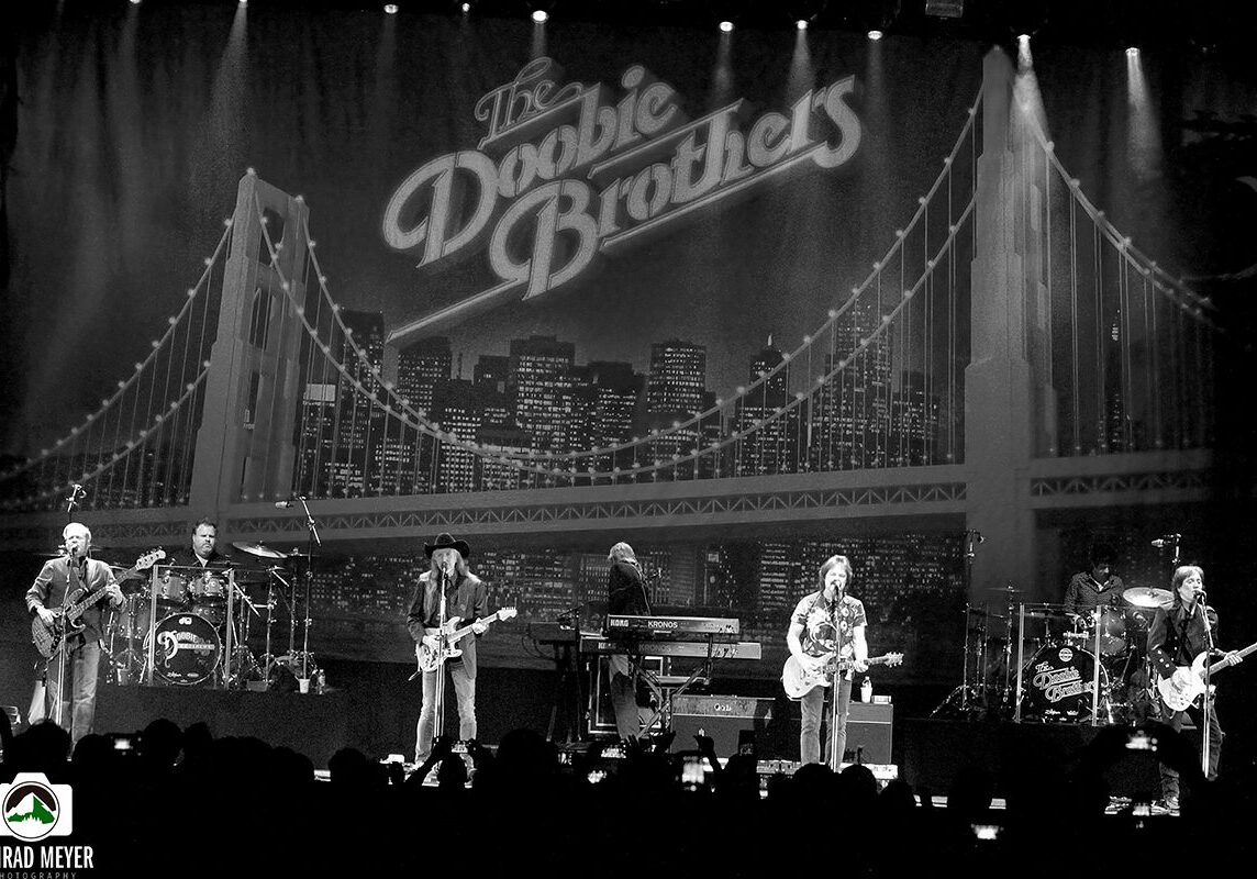 Band performing on stage with city backdrop.