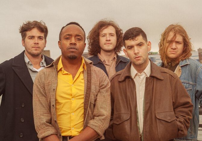Five men standing outdoors, serious expressions.