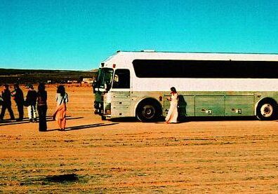 People near a bus in desert landscape.