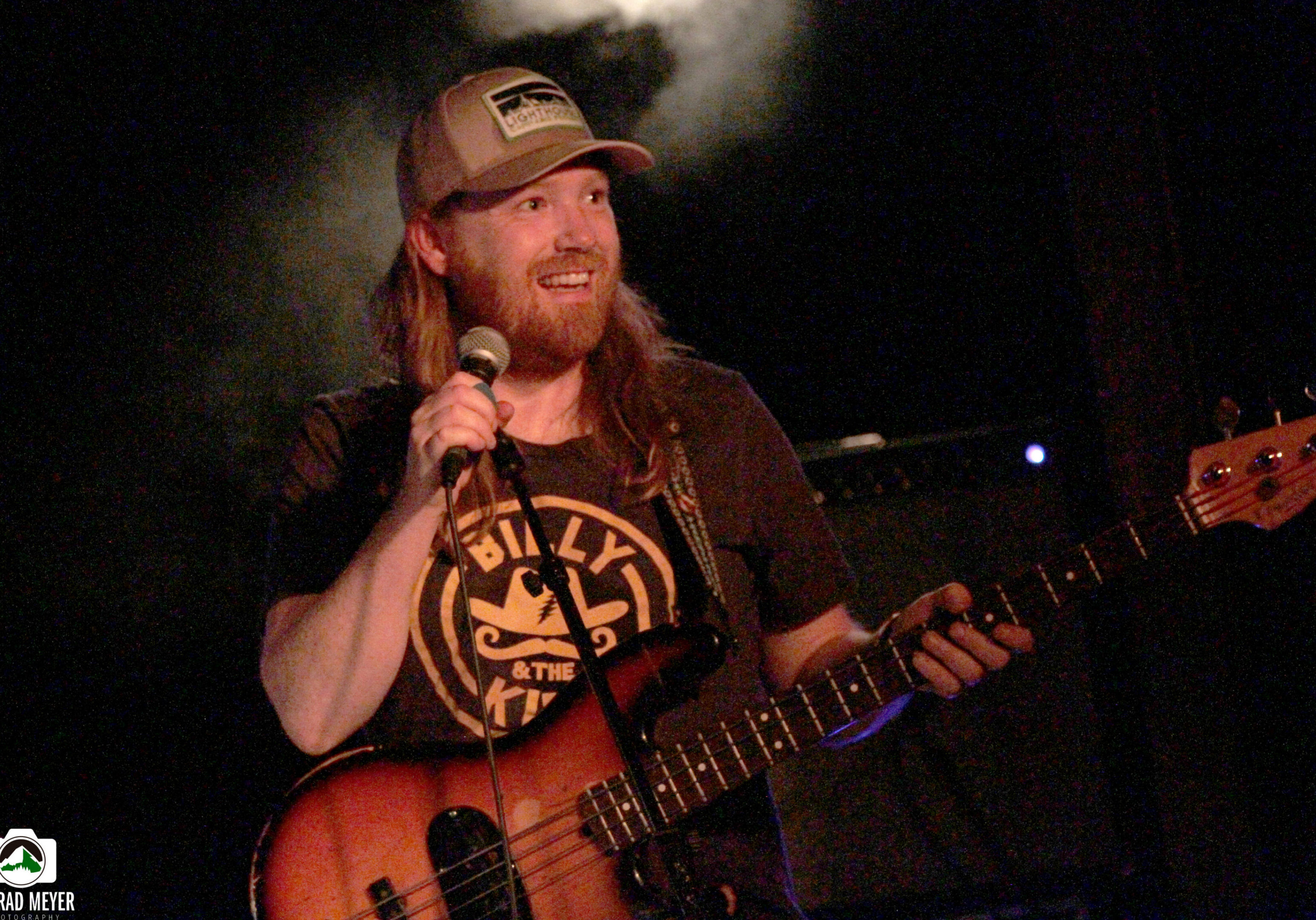 Musician smiling while holding microphone and guitar.