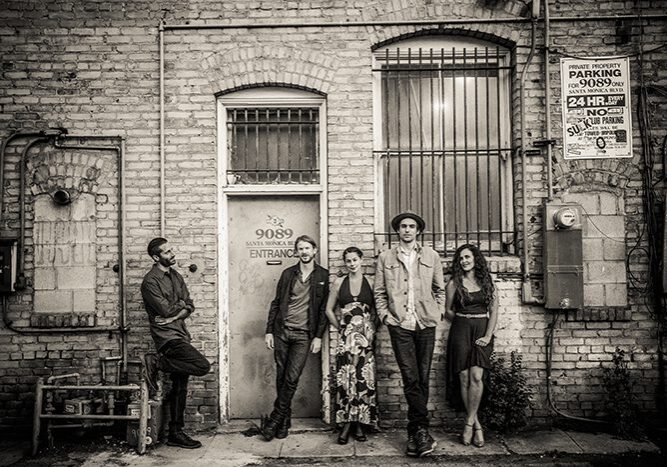 Five people posing against brick wall.