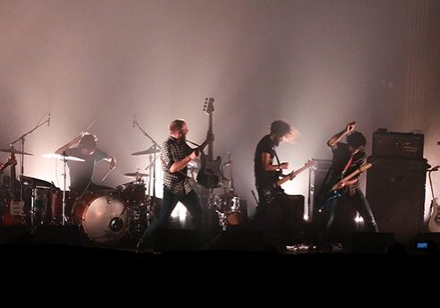 Band performing on stage with dramatic lighting.