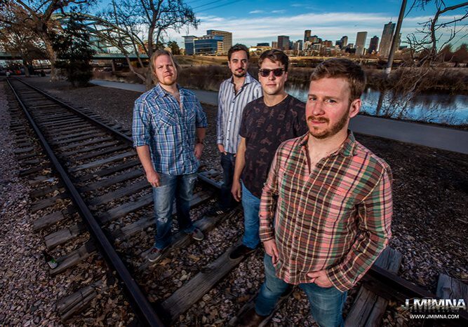 Four men standing on railroad tracks outdoors.